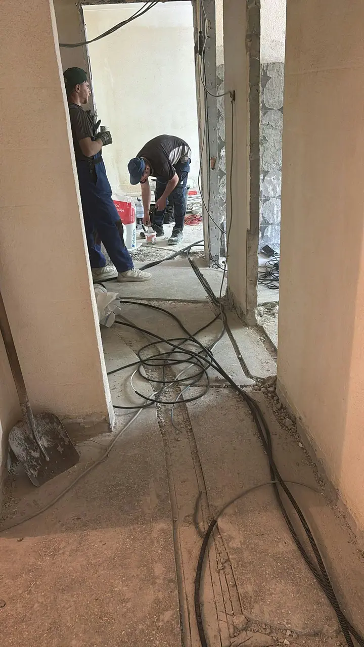 Doi oameni la lucru într-un hol, cu cabluri întinse pe pardoseală